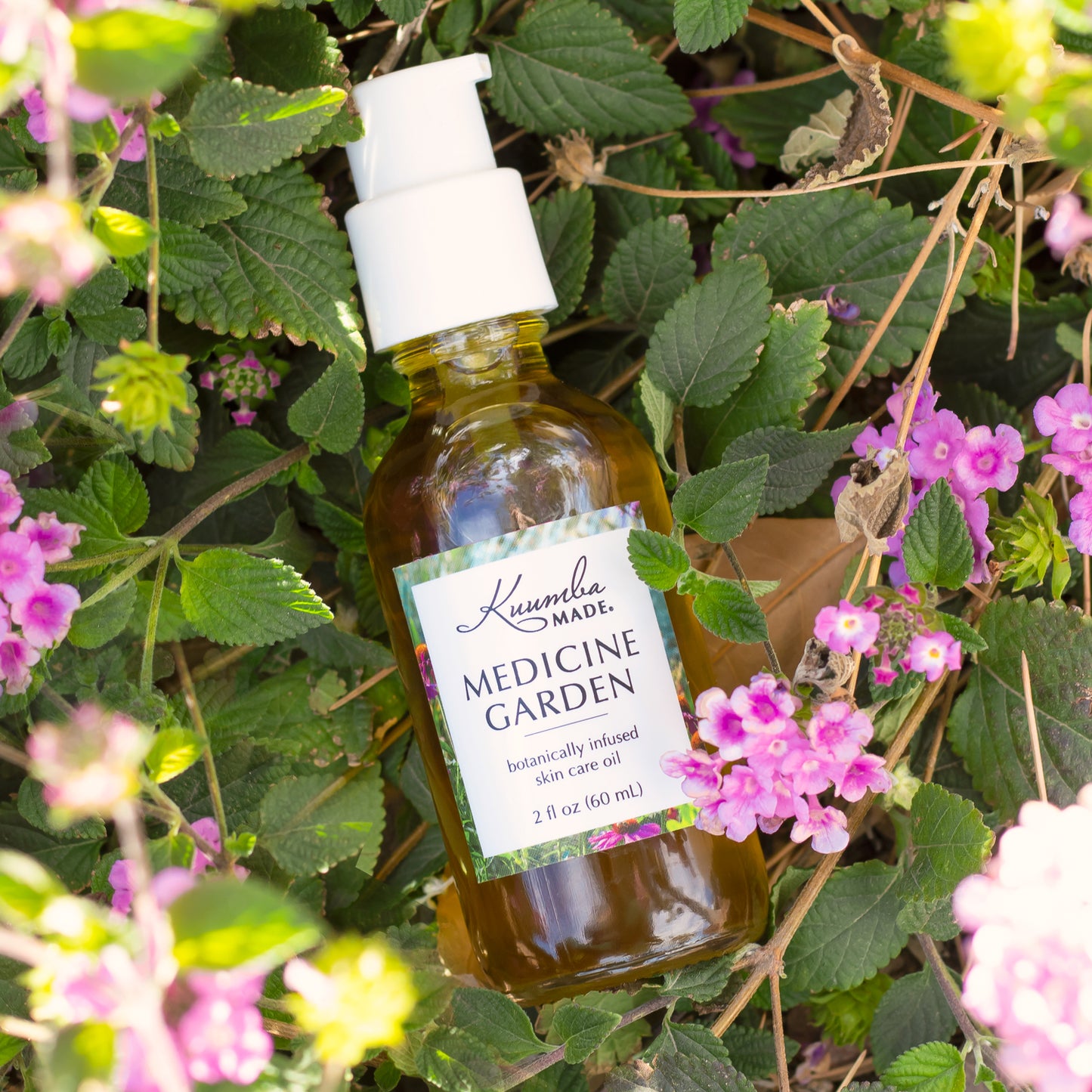 Medicine Garden Botanically Infused Skin Care Oil 2oz bottle from Kuumba Made surrounded by pink flowers.